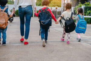 Image of a mother walking with 4 kids with backpacks. Showing the kind of support you can receive from parent coaching and educational consulting in Washington DC, Baltimore, and Columbia, MD.